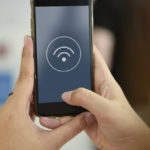 Une personne tient un téléphone portable et à son centre se trouve un logo Wi-Fi.