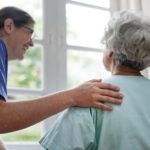 Une aide-soignante qui sourit a une personne âgée en intérieur